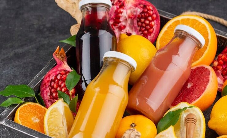 Des Boissons naturelles à base de fruits et légumes posés dans un panier à côté de quelques fruits