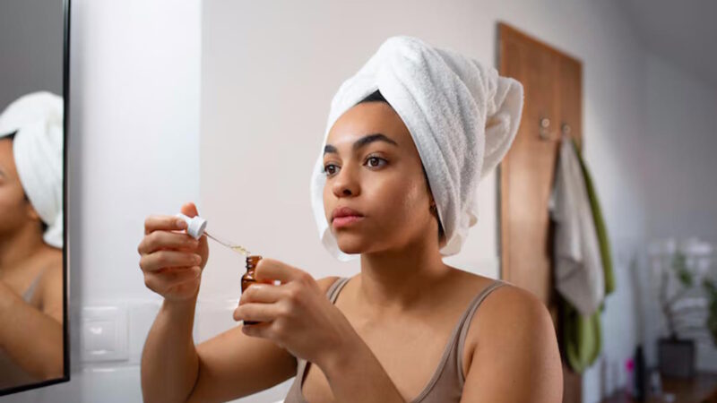 Une femme qui applique de l'huile sur son visage avec les cheveux sous une serviette